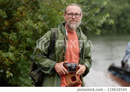 Waist up portrait of smiling male tourist with vintage camera looking at camera while travelling outdoors in nature 119618584