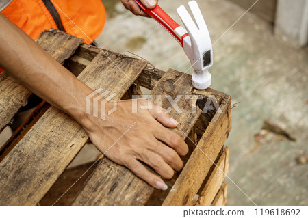 Workers in safety vest using hammer to to work assembling pallet parts 119618692