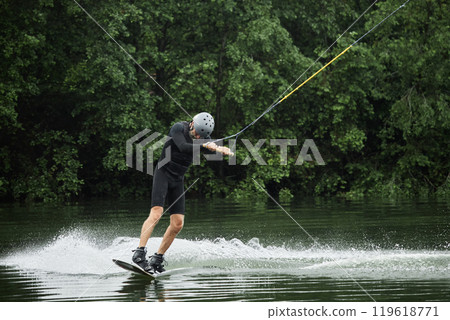 Wide angle action shot of active senior man enjoying wakeboarding on scenic forest lake with wave trail copy space Wide angle action shot of active senior man enjoying wakeboarding on scenic forest lake with wave trail copy space 119618771