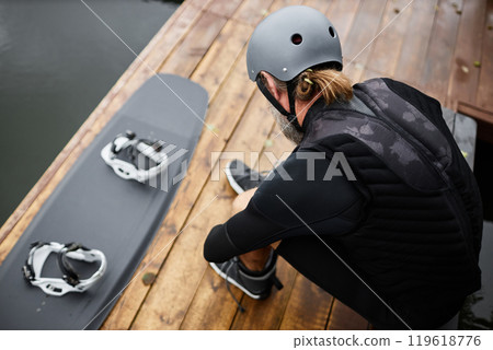 Top view of unrecognizable man putting on wakeboarding gear on wooden pier preparing for water sports outdoors copy space Top view of unrecognizable man putting on wakeboarding gear on wooden pier preparing for water sports outdoors copy space 119618776