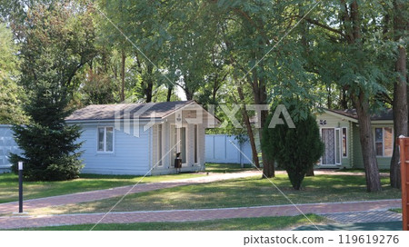 Blue and green wooden one-story country houses among green trees and vegetation, a quiet street with cozy wooden cottages among a beautiful forest, rest in huts in nature 119619276