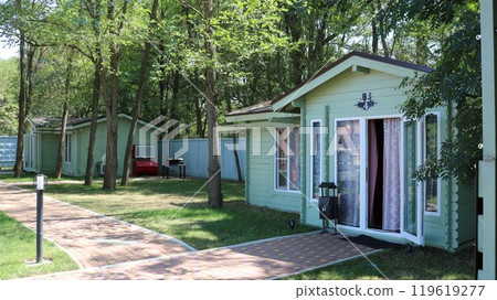Light green one-story wooden country houses among green trees and vegetation, outdoor recreation in cozy wooden cottages among clean air and fresh forest 119619277