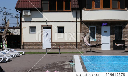Two-story modern brick beige house next to a swimming pool with bright blue clear water and white sun loungers, a place to relax in a hotel by the pool without people Two-story modern brick beige house next to a swimming pool with bright blue clear water and white sun loungers, a place to relax in a hotel by the pool without people 119619278