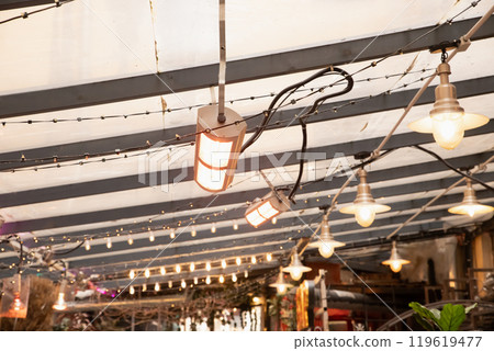 infrared lamp, infrared heater or IR lamps. Soft warm lights illuminate an outdoor dining area under a draped canopy during the evening, creating a cozy atmosphere for guests 119619477