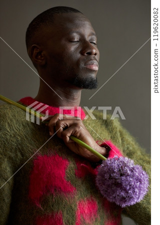 Side view fashion portrait of young African American man holding pink flowers in bloom and wearing soft fuzzy sweater shot on film in studio Side view fashion portrait of young African American man holding pink flowers in bloom and wearing soft fuzzy sweater shot on film in studio 119620082