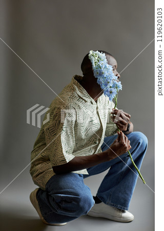 Minimal artistic shot of African American man holding delicate exotic flower and hiding face shot on film with grain Minimal artistic shot of African American man holding delicate exotic flower and hiding face shot on film with grain 119620103