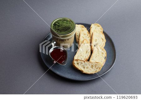 Delicate chicken liver mousse on a ceramic plate next to pieces of white baguette and berry jam 119620693