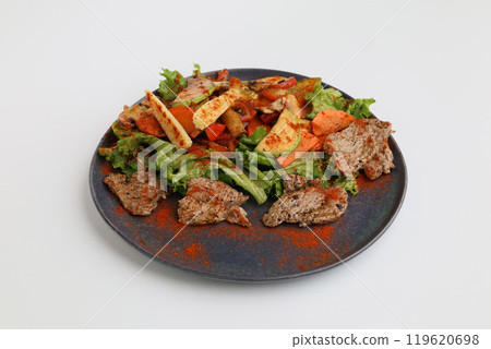 Salad with grilled veal and vegetables on a dark plate on a white background, restaurant serving 119620698