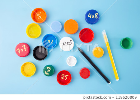 bottle caps with multiplication exercises on blue background, practice for kids, Flat lay educational concept. step in creative process, DIY, effective to learn, master times tables. 119620809
