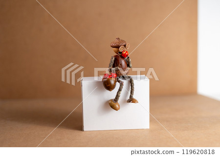 Handmade acorn figurine holding berry basket, seated on white box, natural materials, whimsical autumn decoration, creative DIY project Handmade acorn figurine holding berry basket, seated on white box, natural materials, whimsical autumn decoration, creative DIY project 119620818