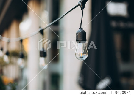 Hanging Outdoor String lights. Decorative Outdoor Street electric garland. Old light bulbs. Lamp hang in the yard. Terrace concept. Festoon string lights decoration at the party Hanging Outdoor String lights. Decorative Outdoor Street electric garland. Old light bulbs. Lamp hang in the yard. Terrace concept. Festoon string lights decoration at the party 119620985