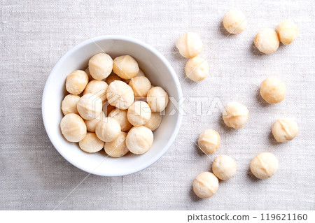 Macadamia nuts, roasted and salted, in a white bowl on linen fabric. Also known as Queensland nut, bush nut, maroochi nut, bauple and Hawaii nuts. Ready-to-eat snack nuts. Close-up, from above. Photo 119621160