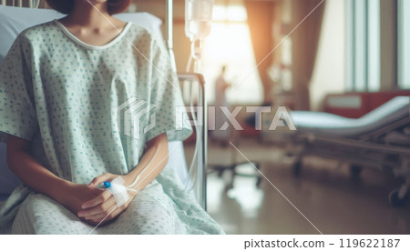 Patient in hospital gown sitting on bed with IV drip in hand. Medical care and recovery concept in healthcare facility 119622187