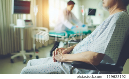 Elderly patient in hospital gown sitting in wheelchair with doctor in background. Healthcare and patient care concept 119622192