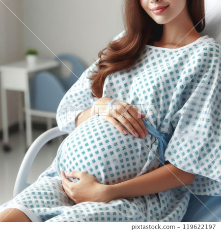 Pregnant woman in hospital gown holding her belly while sitting in a hospital bed. Maternity and childbirth concept 119622197
