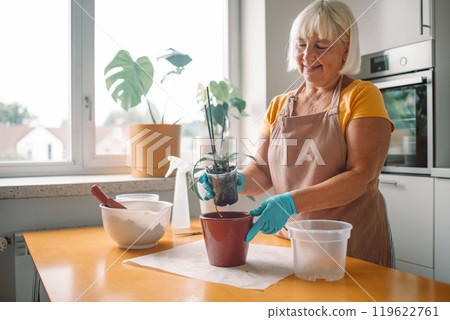 Gardening home. Woman farmer preparing to replant orchid plants by use a shovel to scoop the soil into the pot. Indoor gardening hobbies and jobs indoor plants at home. 119622761