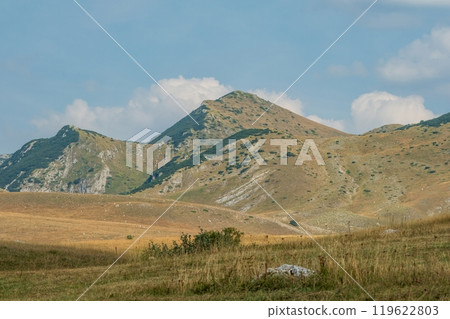 Grassy mountain slopes with rocky terrain under blue sky. Durmitor National Park Montenegro Grassy mountain slopes with rocky terrain under blue sky. Durmitor National Park Montenegro 119622803