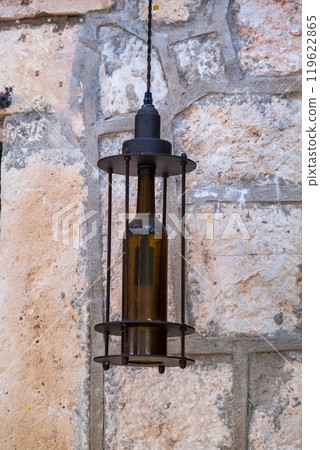 Rustic bottle-shaped lantern hanging on stone wall 119622865