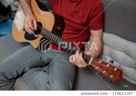 Guitarist paying a acoustic guitar in studio. portrait Male musician sitting on sofa and playing music instrument 119623107