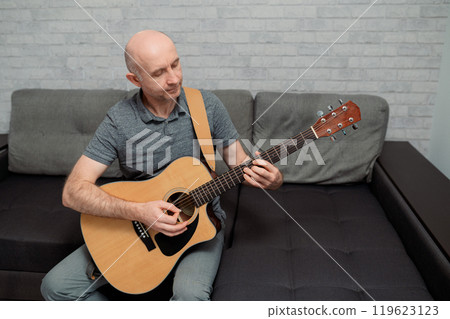 Guitarist paying a acoustic guitar in studio. portrait Male musician sitting on sofa and playing music instrument 119623123