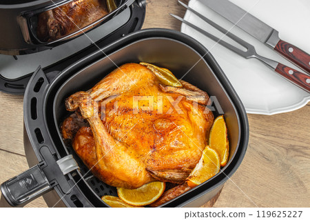 delicious roasted whole chicken with oranges in air fryer on a wooden table. top view delicious roasted whole chicken with oranges in air fryer on a wooden table. top view 119625227