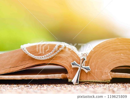 Shiny metal cross leaning against an old open book symbolizing the spread of Jesus Christs love among Christians reflecting faith devotion and the importance of Christian teachings. 119625809