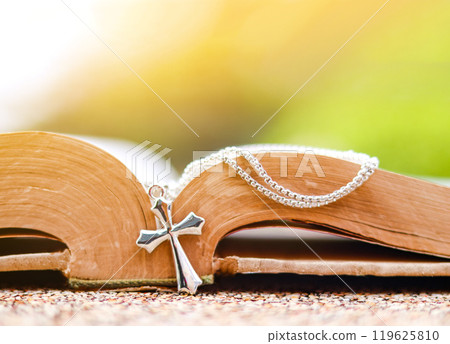 Shiny metal cross leaning against an old open book symbolizing the spread of Jesus Christs love among Christians reflecting faith devotion and the importance of Christian teachings. 119625810