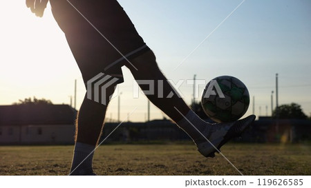 Legs of young man kicking ball at green field. Male feet of professional footballer juggling soccer ball on stadium at sunset. Sportsman practicing tricks outdoor. Concept of a freestyle football Legs of young man kicking ball at green field. Male feet of professional footballer juggling soccer ball on stadium at sunset. Sportsman practicing tricks outdoor. Concept of a freestyle football 119626585