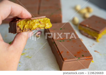 Piece of trend Dubai chocolate with pistachio paste and kataifi dough in woman hand. Confectionery handmade sweets at home in the kitchen.  119626669