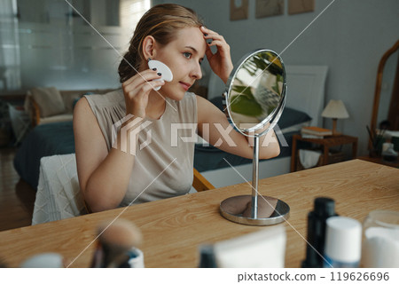 Young Woman Applying Skincare Product in Living Area 119626696