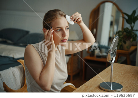 Young Woman Carefully Applying Facial Skincare Product 119626697