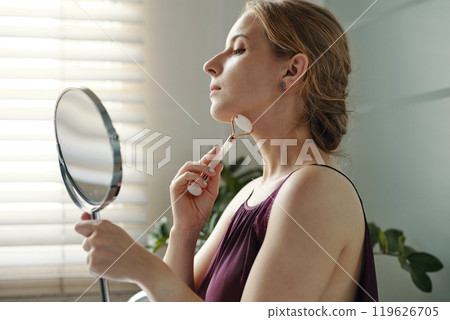 Practicing Self-Care with Facial Roller by Window 119626705
