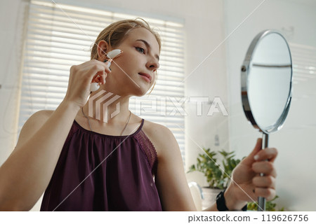 Woman Using Skincare Device in Well-Lit Room 119626756