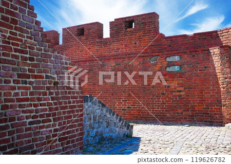 Old red brick fortress wall with two turrets under blue sky on a sunny day Old red brick fortress wall with two turrets under blue sky on a sunny day 119626782