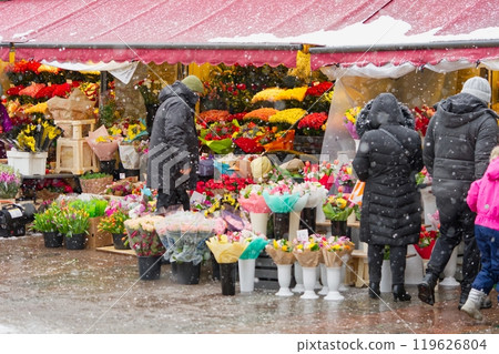 Customers at a colorful flower shop on a snowy day in the city. 119626804