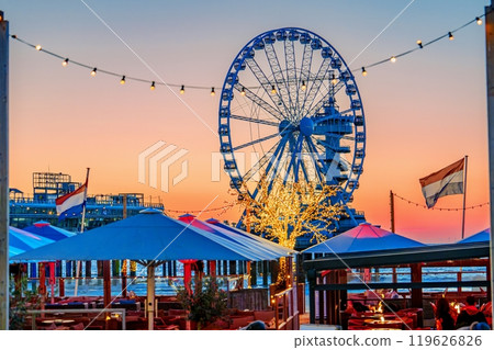 Stunning Ferris wheel illuminated at sunset with vibrant sky and restaurant view at amusement park 119626826