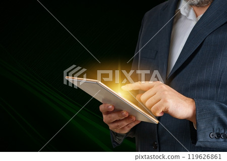 Businessman with Tablet Illuminated by Bright Light in Dark Room Businessman with Tablet Illuminated by Bright Light in Dark Room 119626861
