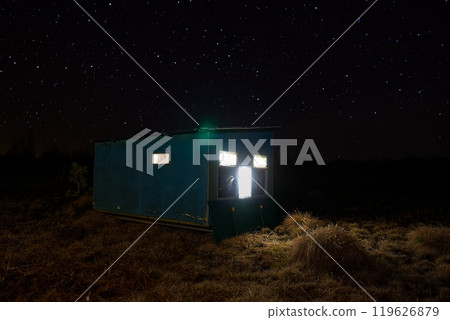 Small Wildlife Photo Hide in the middle of a grass field at night with the light on and a starry sky. 119626879