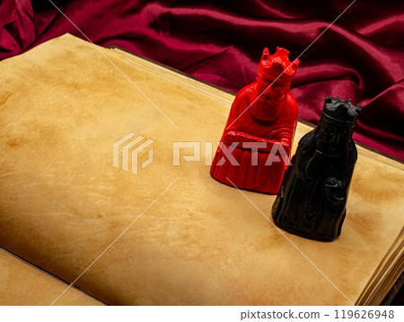 yellowed medieval ancient blank book open on a table with small statues representing figures of the King and Queen. yellowed medieval ancient blank book open on a table with small statues representing figures of the King and Queen. 119626948