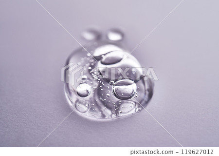 A drop of serum on a purple background. Texture of a cosmetic product. A drop of serum on a purple background. Texture of a cosmetic product. 119627012