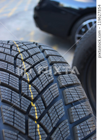 Snowflake pictogram to show wear level on new winter tire in front of a defocused car at tire service. Seasonal tire change stock image. Design of non studded winter tires Snowflake pictogram to show wear level on new winter tire in front of a defocused car at tire service. Seasonal tire change stock image. Design of non studded winter tires 119627854