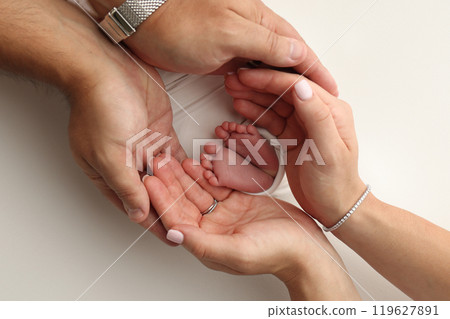 The palms of the parents. A father and mother hold the feet of a newborn child in a white blanket on a white background.. The feet of a newborn in the hands of parents. Photo of foot, heels and toes The palms of the parents. A father and mother hold the feet of a newborn child in a white blanket on a white background.. The feet of a newborn in the hands of parents. Photo of foot, heels and toes 119627891
