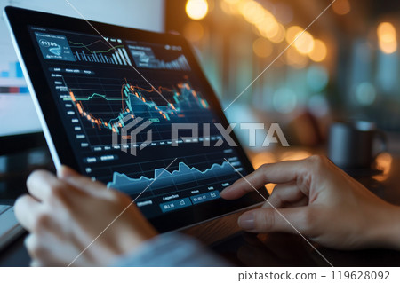A person using a digital tablet to manage their diversified investment portfolio.A person is using their hand to interact with a tablet that displays a graph 119628092
