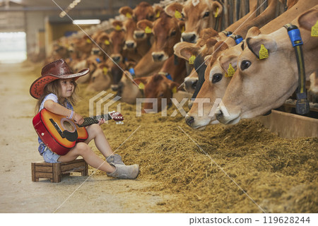 Charming child in a cowboy costume sings for cows on a farm in Denmark Charming child in a cowboy costume sings for cows on a farm in Denmark 119628244