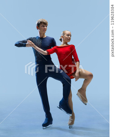 Two young, elegant figure skaters in perfect sync, executing complex pose on ice against cold blue background. Choreography on ice. Two young, elegant figure skaters in perfect sync, executing complex pose on ice against cold blue background. Choreography on ice. 119628384