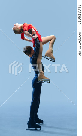Portrait of figure skating couple executing dramatic overhead lift against cold blue background, combination of power and grace. Portrait of figure skating couple executing dramatic overhead lift against cold blue background, combination of power and grace. 119628385