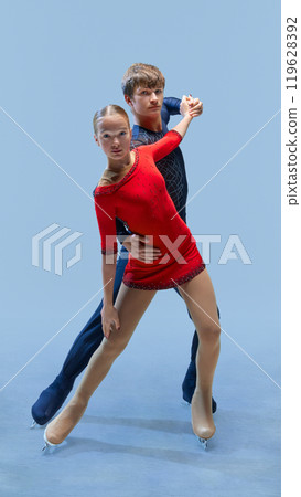 Figure skating pair in intense and synchronized pose againstcold blue background, show their focus and grace as they glide on ice. 119628392