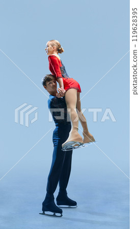 Graceful male and female figure skating pair executing dynamic lift on ice against cold blue background. Precision and athleticism of figure skating in competition. Graceful male and female figure skating pair executing dynamic lift on ice against cold blue background. Precision and athleticism of figure skating in competition. 119628395