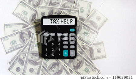 The display of the calculator says Tax Help . Dollars are lying on a white background . 119629031