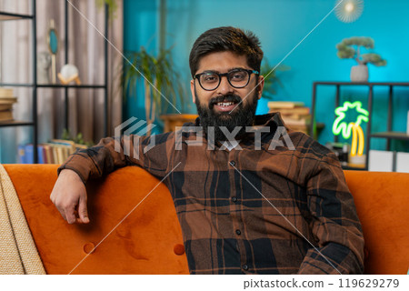 Portrait of happy Indian man looking at camera and smiling at home relaxing wearing eyeglasses Portrait of happy Indian man looking at camera and smiling at home relaxing wearing eyeglasses 119629279
